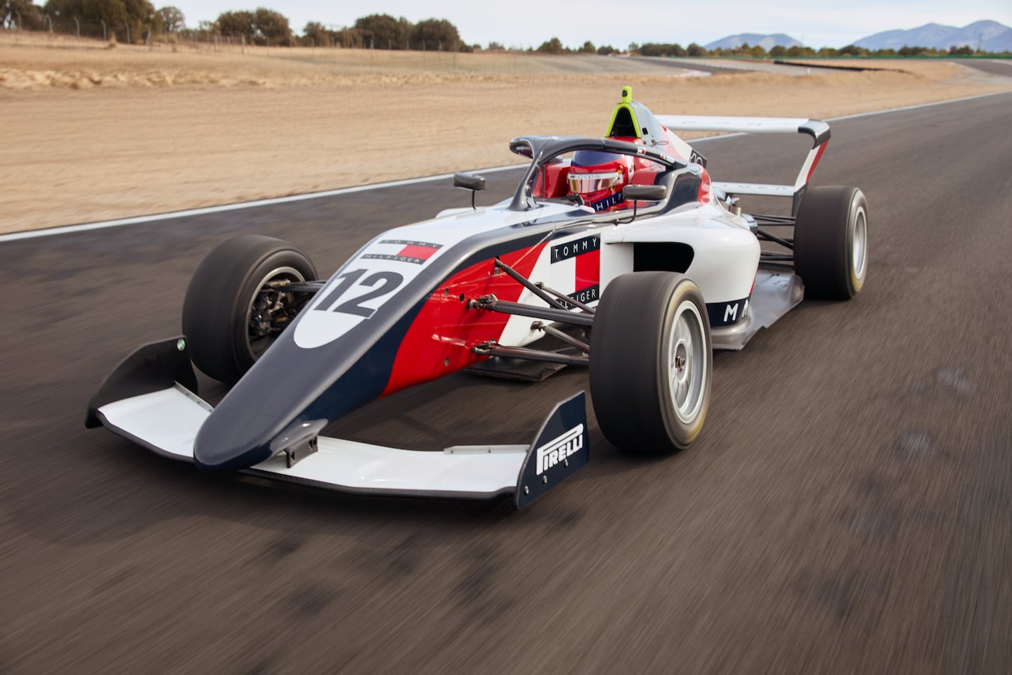 A Tommy Hilfiger branded Formula 1 car driving down a test track.