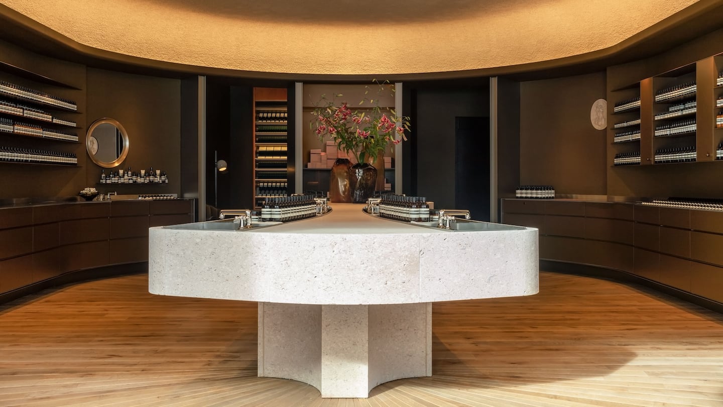 Aesop Regent Street, London, with a central counter displaying products, with sinks, and shelves displaying products on the walls.